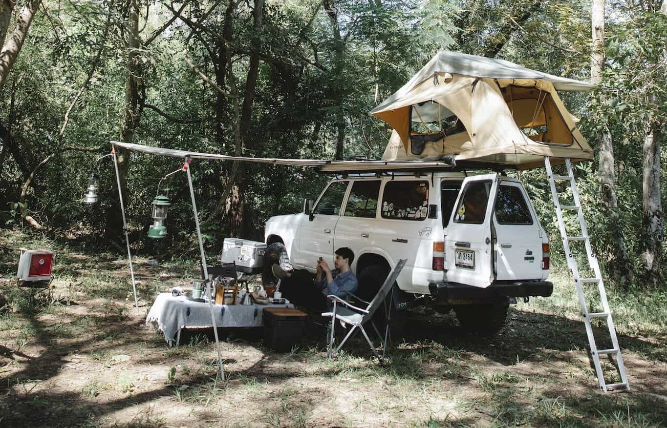 Camping car with tent on roof parked in forest in sunlight